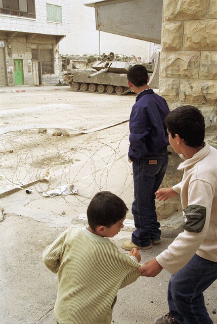 Palestinski otroci zmerjajo izraelske vojake, ki so se s svojimi tanki in oklepniki razmestili po mestu.