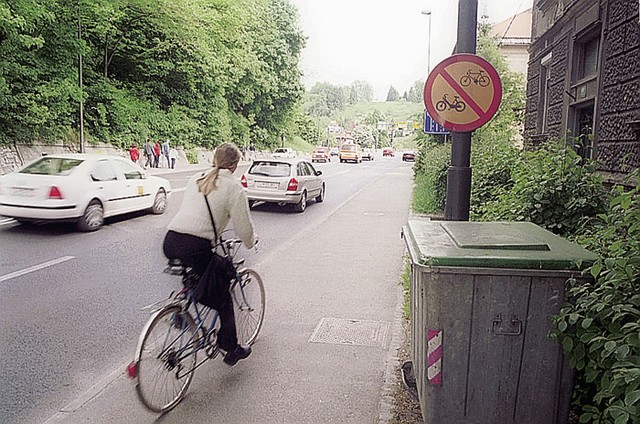 Tako kakor po presenetljivo številnih ulicah v središču Ljubljane, je vožnja kolesarjem prepovedana tudi po Karlovški cesti. Posebnost Karlovške je, da se nekaj deset metrov naprej od znaka na fotografiji pojavi prava pravcata kolesarska steza. Nikjer ni nobenega znaka, da prepoved vožnje za kolesarje ne velja več, prav tako ni jasno, kako naj bi kolesar sploh prišel do tja.
