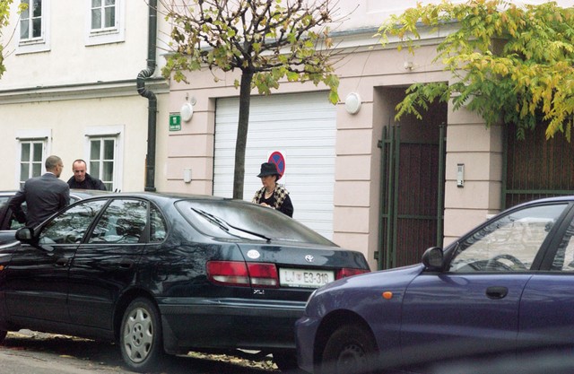 Zadovoljna gospa Rupel med vstopanjem v službeni avto svojega moža pred svojo hišo