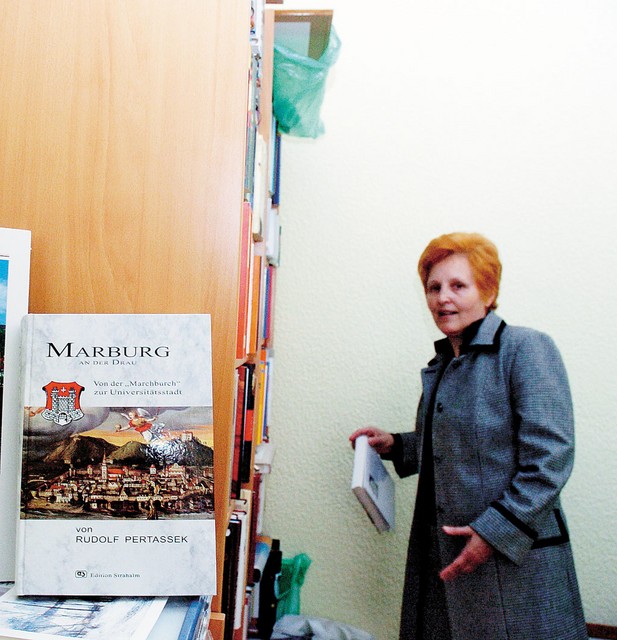 Veronika Haring pred društveno knjižno polico; v ospredju Pertasskova knjiga o nemški zgodovini Maribora