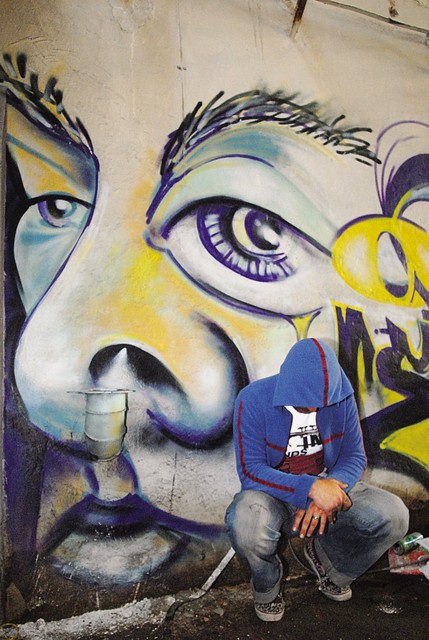 Grafitar Seyo pred svojo umetnino na zidu propadle tovarne Rog