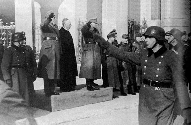 Slavnostni mimohod domobranskih čet pred Uršulinsko cerkvijo v Ljubljani, 30. januarja 1945. Na piedestalu stojijo: Leon Rupnik, poveljnik domobranskih enot, škof Gregorij Rožman in Erwin R&#246sener, poveljnik nemških čet.