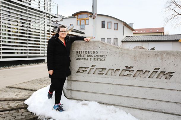 Nadja Kramer, slovenska aktivistka iz Dobrle vasi, pred napisom slovenskega podjetja Sienčnik, ki ji daje kruh.
