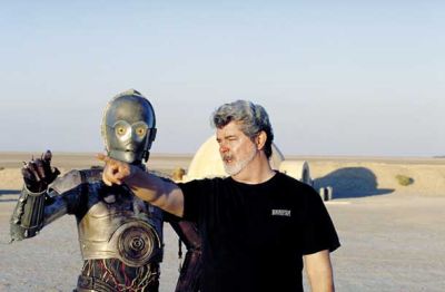 Oče Vojne zvezd George Lucas usmerja igralca Anthonyja Danielsa, ki mu je pripadla vloga droida C-3PO, na snemanju filma Vojna zvezd: Napad klonov (Epizoda II, 2002) v tunizijski puščavi