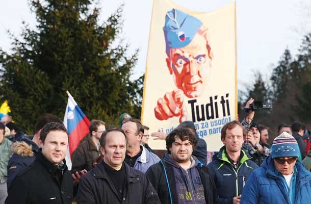 Na domnevno spontanem protestu proti namestitvi beguncev v Šenčurju: V prvih vrstah poslanca SDS Žan Mahnič in Branko Grims, v ozadju domobranski plakat iz leta 1945 – poziv k akciji. Leta 1945 je pozival k boju proti komunistom, leta 2016 pa k boju proti beguncem.