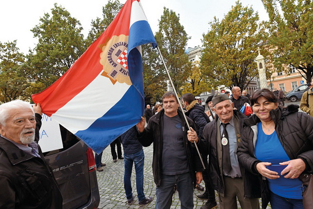 Ustaška zastava in v uniformo hrvaških domobrancev, redne vojaške enote NDH oblečen posameznik pred mariborsko stolnico, v kateri jjee ppootteekkaallaa mmaaššaa ob pokopu žrtev Hude Jame 