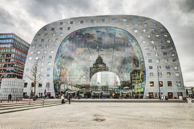 Markthal, Rotterdam. Ogromno tržno dvorano s strani zaobjameta stavbna trakta, ki imata v prerezu obliko podkve. V notranjosti prodajne paviljone dopolnjujejo gostinski lokali s terasami na strehah.