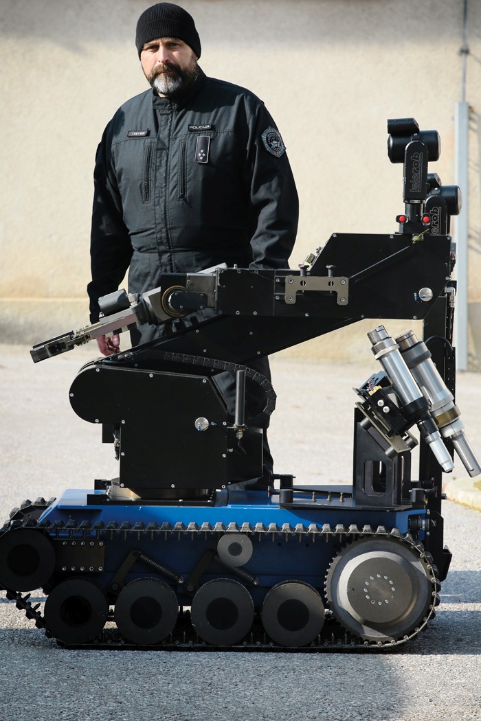 Klemen Pogačar in robot Theodor, ki ga spremlja na vseh nevarnih nalogah. Opremljen je s kamero, kleščami ter vodnim topom in topom za trde izstrelke, nanj je mogoče namestiti tudi rentgen. Gre za resen stroj. Kot pravi Pogačar, si lahko v kakšno tanjšo steno kar sam naredi vrata, avto lahko premakne tudi ob zategnjeni ročni zavori.