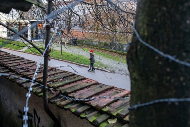 Otrok se na skiroju pelje ob reki pred Avtonomno Tovarno Rog, ki je deloma obdana z bodečo žico, a ne da bi se zaščitila pred zunanjim svetom, temveč kot kritika postavitvi bodeče žice na slovensko-hrvaški meji. Avtonomna Tovarna ROG, odprta za različne kulture, je edino kulturno območje v Ljubljani, ki na spletni strani uporablja tudi arabščino.