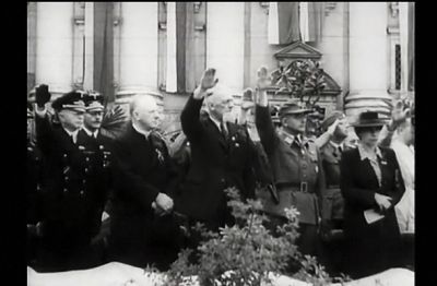 Iztegnjena roka generala Leona Rupnika, poveljnika domobrancev, v pozdrav nacistični Nemčiji. Ob njem stoji škofa Gregorij Rožman, predstavnik RKC. 