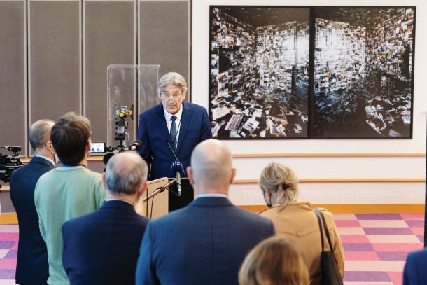 Vasko Simoniti je ponosno odprl razstavo slovenskih avtorjev v Bruslju in omenil prave umetnike, o drugih je molčal (v ozadju ministra delo Diptih iz serije Požrešnost. Gre za fotografijo stanovanja, prelepljenega s fotografijami, posnetimi za Mladino. Delo, ki problematizira inflacijo informacij, je ustvaril Uroš Abram) 