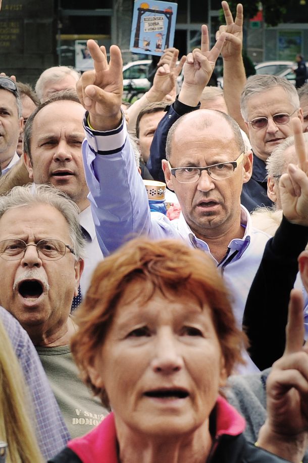 Tudi položaj Janševega brata Rajka Janše kaže, da sedanja slovenska oblast deluje na podlagi tribalnih načel. Kadarkoli se na oblast povzpne Janez Janša, začne v njegovi senci poslovne uspehe nizati njegov brat Rajko Janša, sicer preprodajalec poslovnih daril. (na fotografiji Rajko Janša v sredini z očali in z dvema dvignjenima prstoma na protestu pred sodiščem, ki je obsodilo brata na zaporno kazen v zadevi Patria) / 