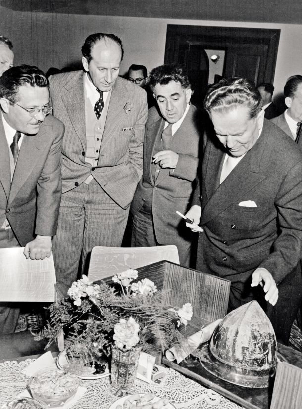 Tito si ogleduje protokolarno darilo, negovsko čelado z Vrhpolja pri Kamniku, ki je nato odpotovalo z njim v Beograd. Fotografija je nastala 23. novembra 1958 na Grmu v Novem mestu. 