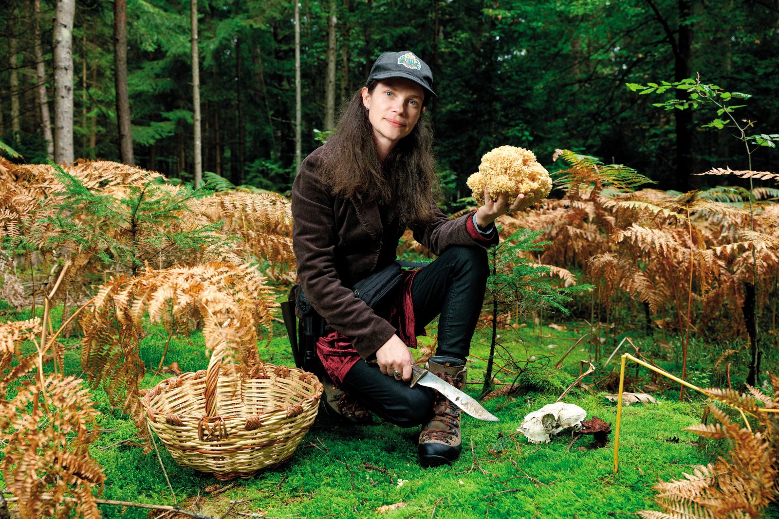 Katarina Grabnar Apostolides v rokah drži veličastnega borovega glivca (Sparassis crispa), v mahu desno od nje pa raste žoltorobi rjavopor (Phaeolus schweinitzii), vendar njegova temna barva kaže, da je že prestar za uporabo.