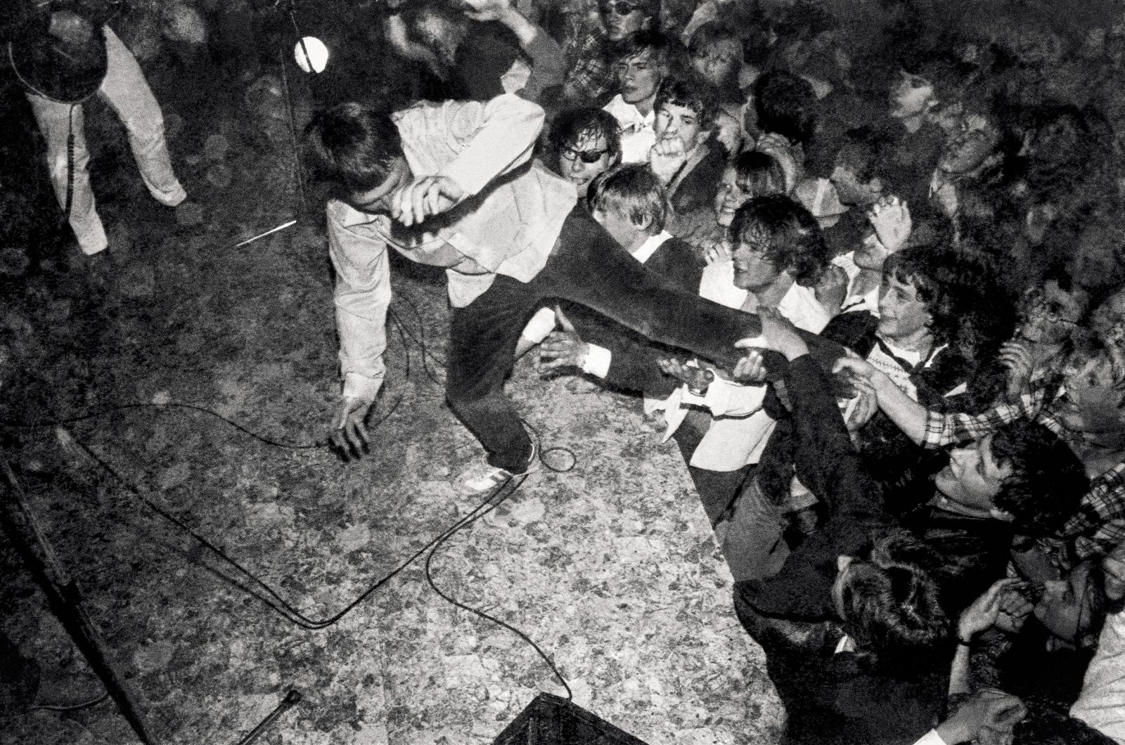 Fotografija Dušana Gerlice prikazuje koncert Pankrtov, ki se je 20. aprila 1979 odvil v menzi študentskega naselja v ljubljanski Rožni dolini.