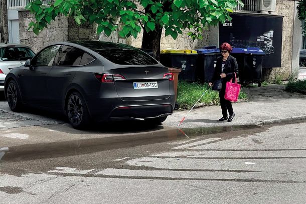 »Fotografija bežigrajskega vsakdana, nastala na začetku Einspielerjeve. Slepa gospa se je najprej zaletela v teslo, parkirano na pločniku, potem je zatavala v lužo na cesti. Prijela sem jo pod roko in peljala okoli. Lastnik mega tesle zaparkira smeti in pločnik … In tako vsak dan ...« 
