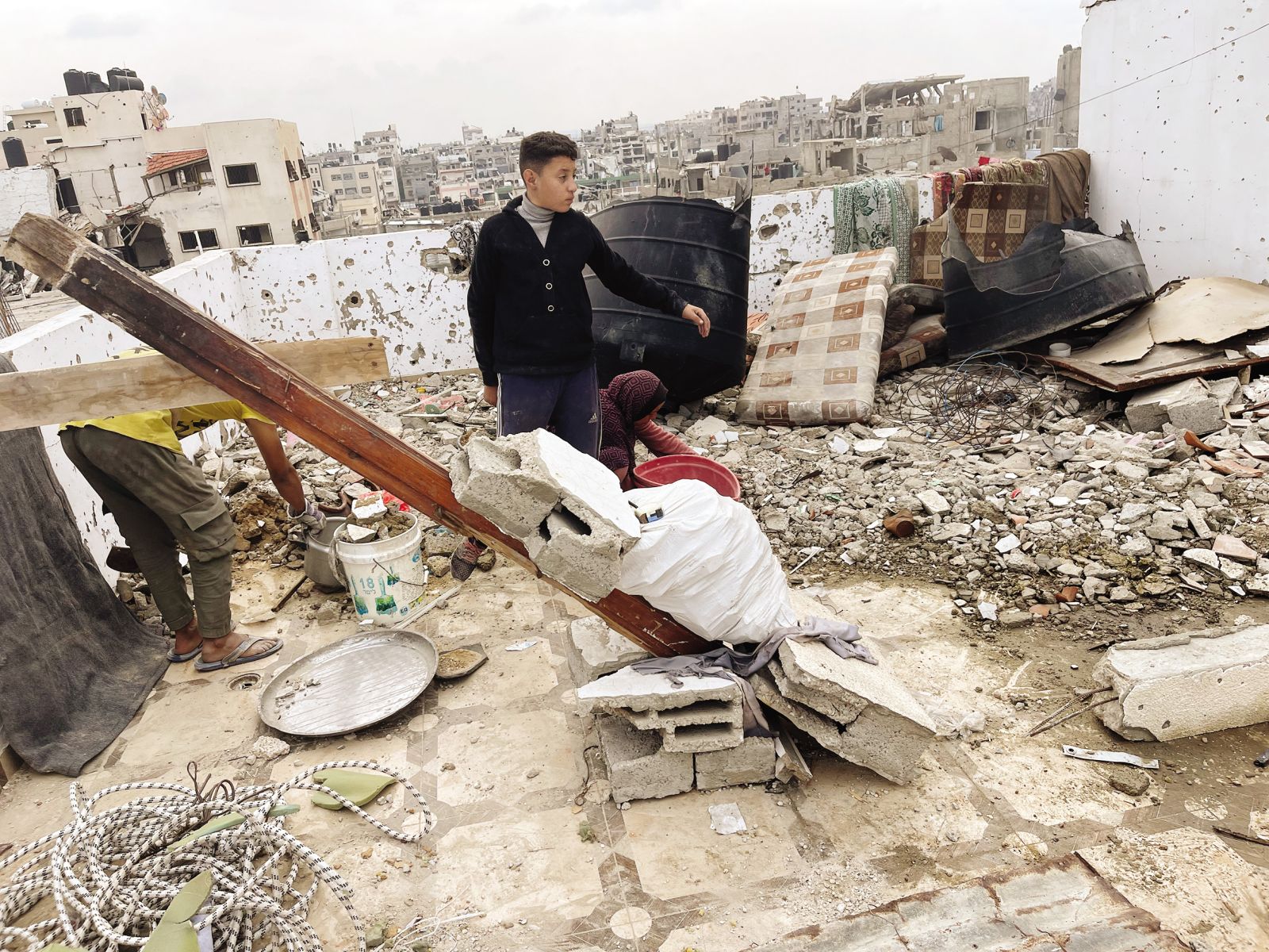 Odstranjevanje ruševin s terase Ahmedovega stanovanja. V ozadju razdejano mesto Gaza.