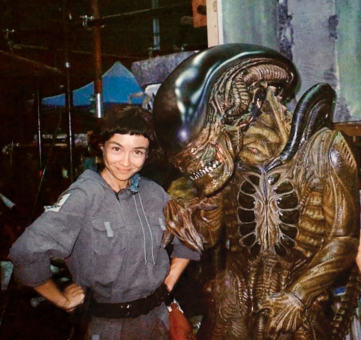 Igralka Sydney Chandler na snemanju serije Alien: Earth (Osmi potnik: Zemlja), v kateri upodablja osrednji lik, transhumanistično robotinjo s človeško zavestjo Wendy, pozira s ksenomorfom, ikonično pošastjo, ki jo po dolgem času ponovno upodablja igralec v kostumu.